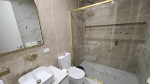 A modern bathroom with a glass-enclosed shower, a white sink, and a toilet.