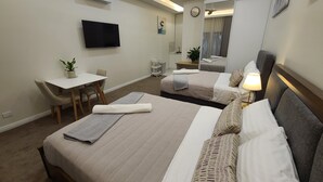 A hotel room with two beds, a desk, a chair, a TV, a mirror, and a ceiling fan.