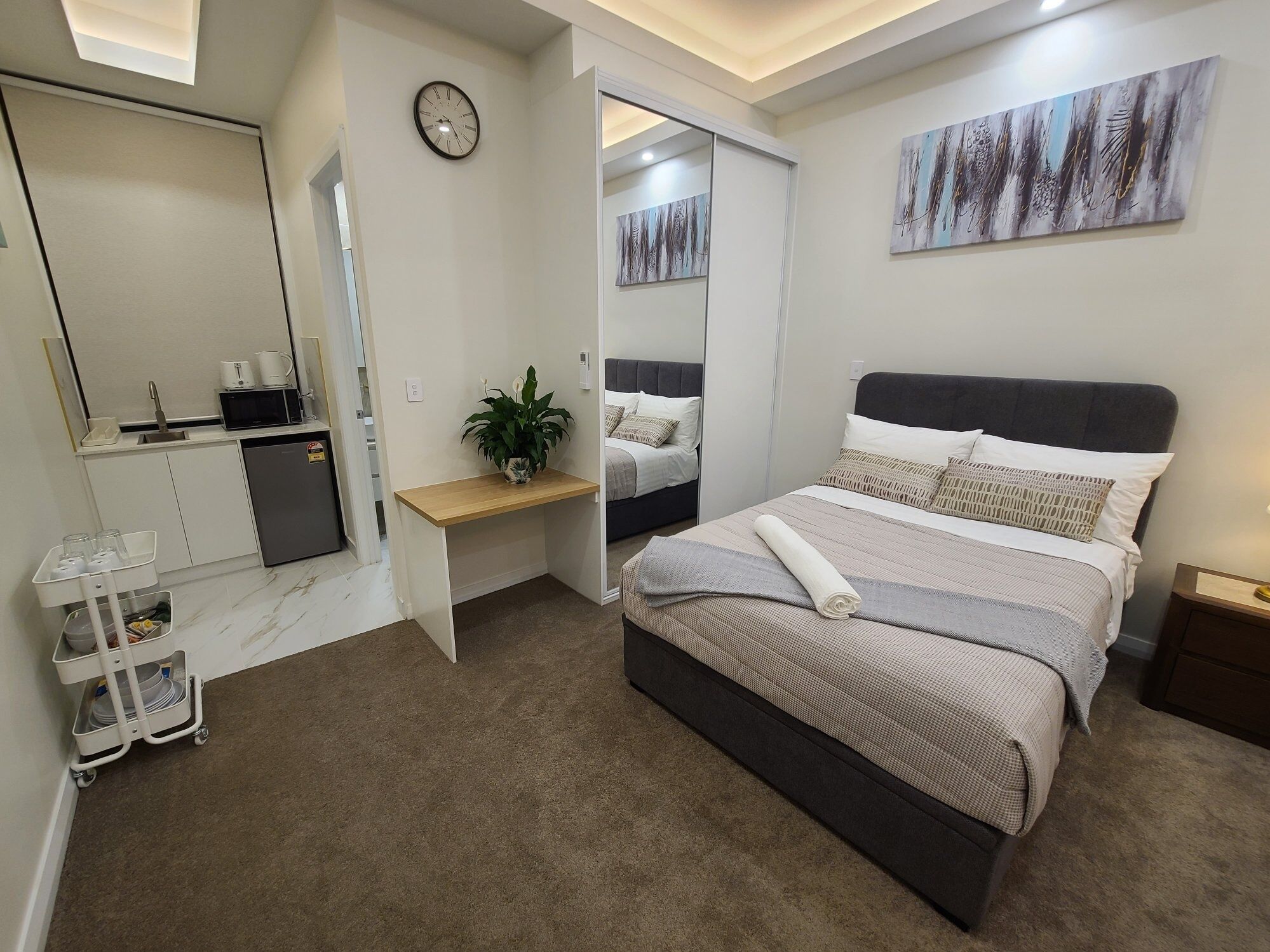 Een moderne slaapkamer met een bed, nachtkastjes, een bureau, een spiegel en een klok aan de muur.
