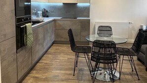 A modern kitchen with a dining area, featuring a built-in oven, a stainless steel sink, and a round glass table with black wire chairs. - Barking Bliss - Bright Apartment With City Views (Barking)