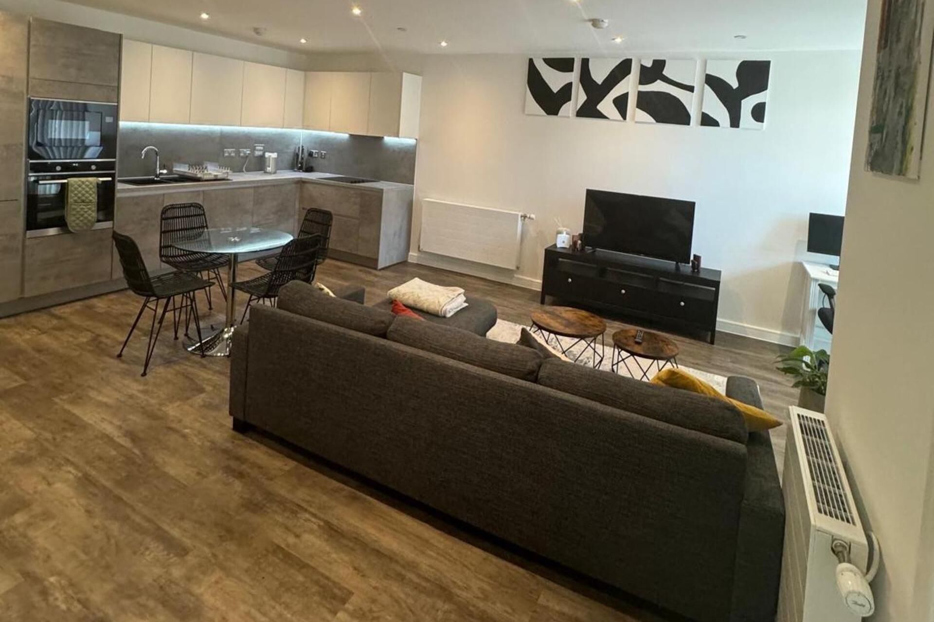 Un salon moderne avec un canapé, un coin repas avec des chaises, une cuisine dotée d’un four encastré et un téléviseur à écran plat.