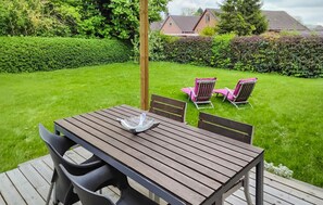 Une terrasse en bois avec une table et des chaises, entourée d’une pelouse bien entretenue et de haies.