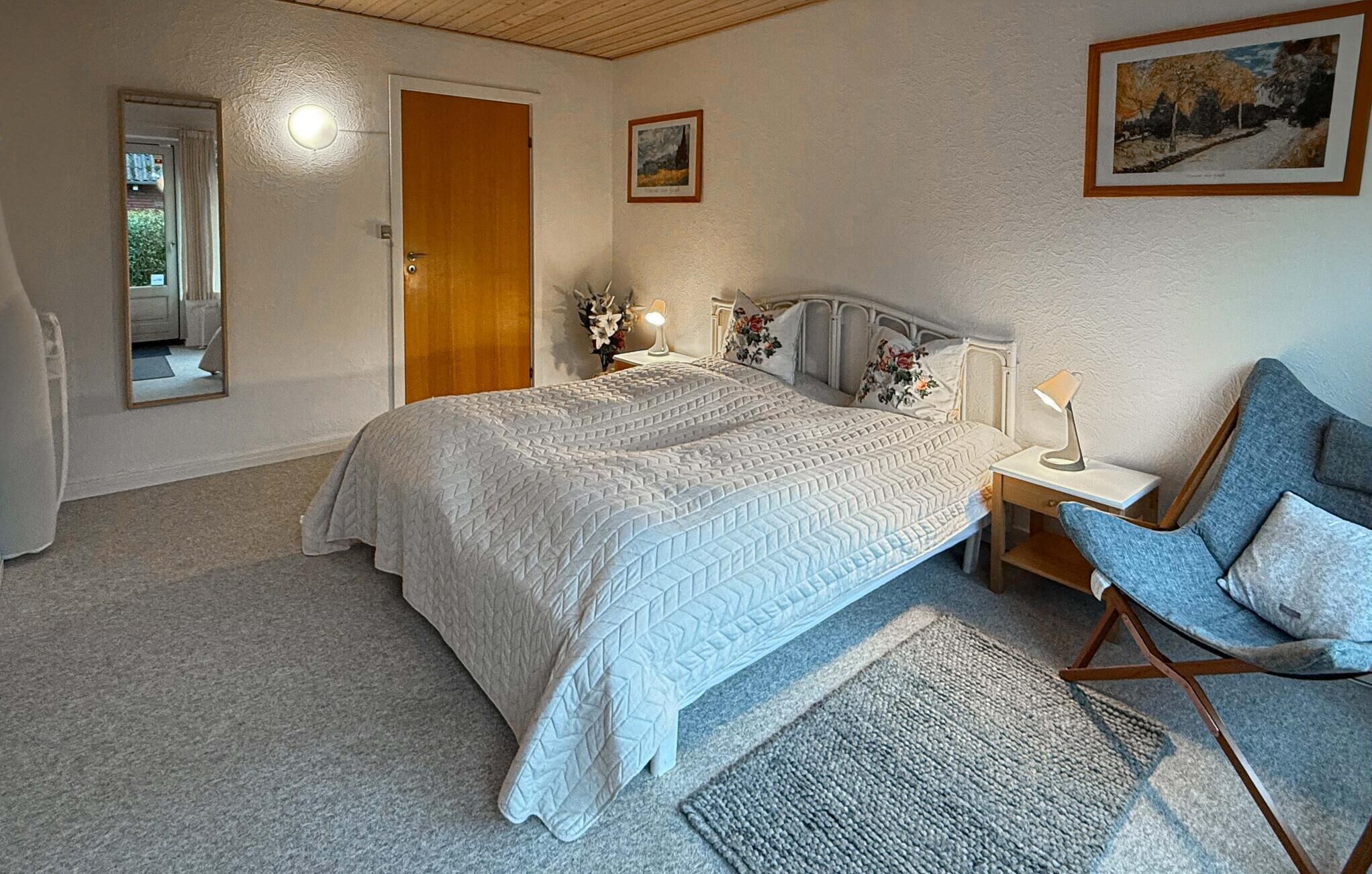 Un dormitorio con una cama grande, una silla, un escritorio, un espejo y dos cuadros en la pared.