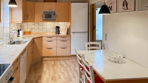 Una cucina compatta con forno a microonde, macchina del caffè e frigorifero. È presente un tavolo da pranzo con sedie e un piccolo oggetto decorativo.