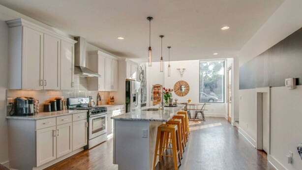 Una cocina moderna con armarios blancos, una isla central con taburetes y un amplio ventanal que proporciona luz natural.