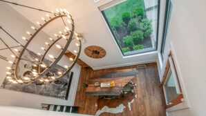 Un interior moderno con una mesa de comedor de madera, una lámpara circular original y vistas a la vegetación a través de un tragaluz.
