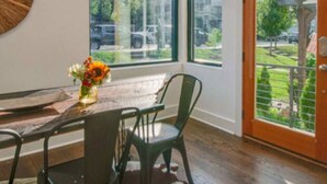 Una habitación con ventanas amplias, una mesa de comedor con sillas, piso de madera y una puerta con vistas al exterior.