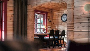 A wooden cabin interior with a dining area featuring a table and chairs, a window with a red frame, and a wall-mounted clock. - Amazing apartment in Bjorli with WiFi (Bjorli)