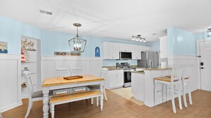 A modern kitchen with white cabinetry, a wooden dining table, and a bar area. - Coastal Comfort with Golf, Pool, Pickle Ball, Tennis Courts (Murrells Inlet)