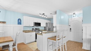 A kitchen with white cabinets, a granite countertop, and a central island with bar stools. - Coastal Comfort with Golf, Pool, Pickle Ball, Tennis Courts (Murrells Inlet)