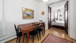 A dining area with a wooden table and chairs, a cityscape poster on the wall, and a red patterned rug on the floor.