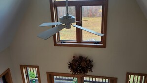Una habitación con ventilador de techo, ventanas amplias y vista a un patio.