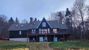 Una casa grande de color oscuro con un balcón destacado y varias ventanas.