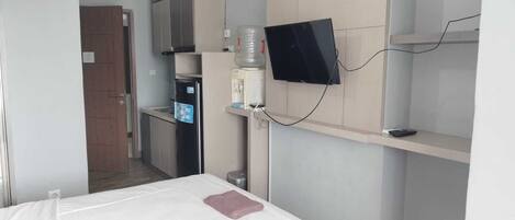 A hotel room with a bed, a TV mounted on the wall, a water dispenser, and a small kitchenette.