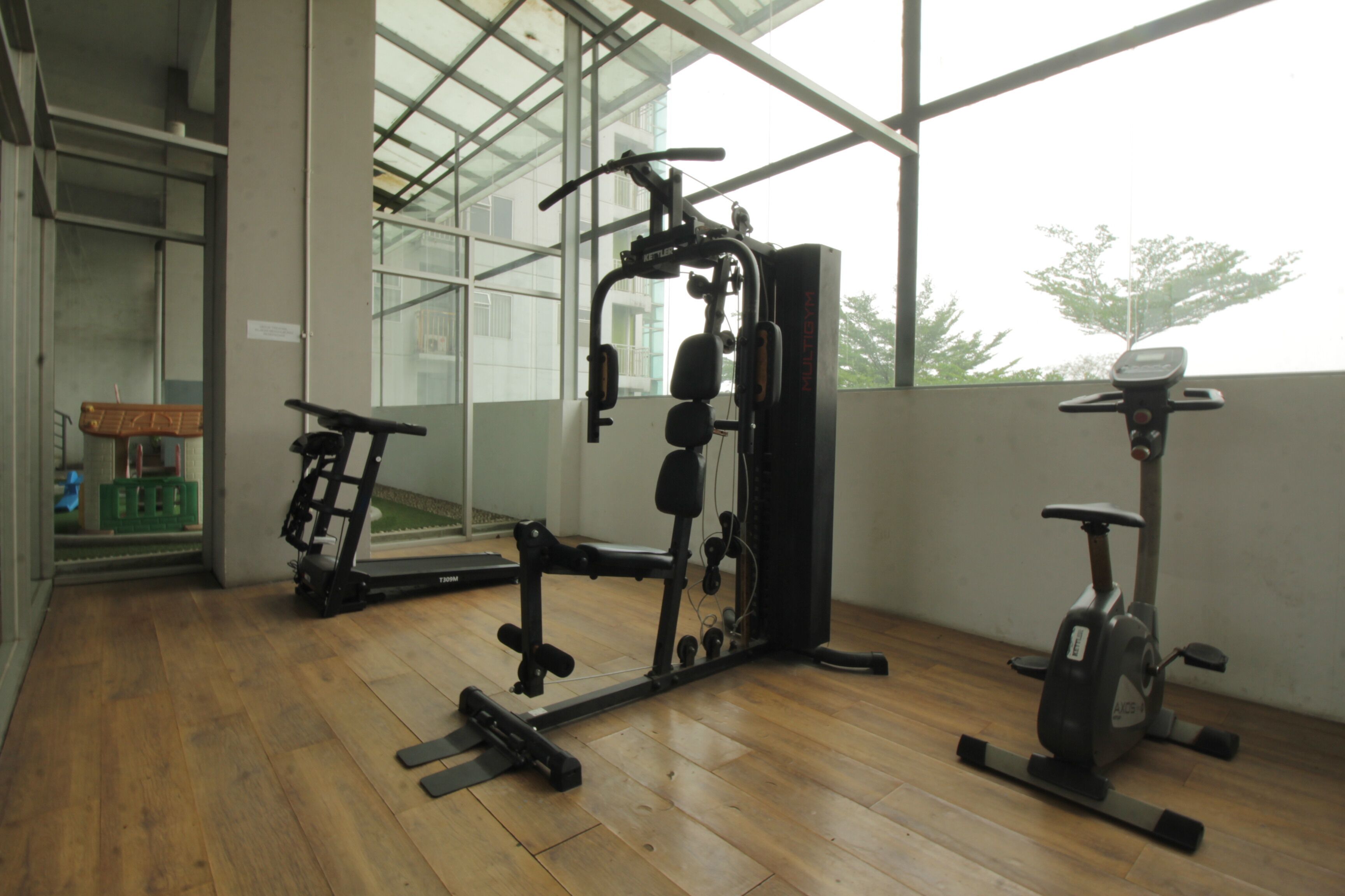 A gym with exercise equipment, large windows, and wooden flooring.