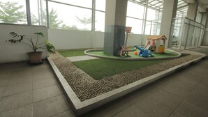Un grand espace intérieur comprenant un petit jardin artificiel, une structure de jeux et une plante en pot.