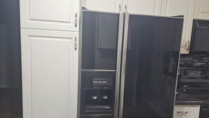 Een keuken met een zwarte koelkast, witte keukenkastjes en een magnetron.