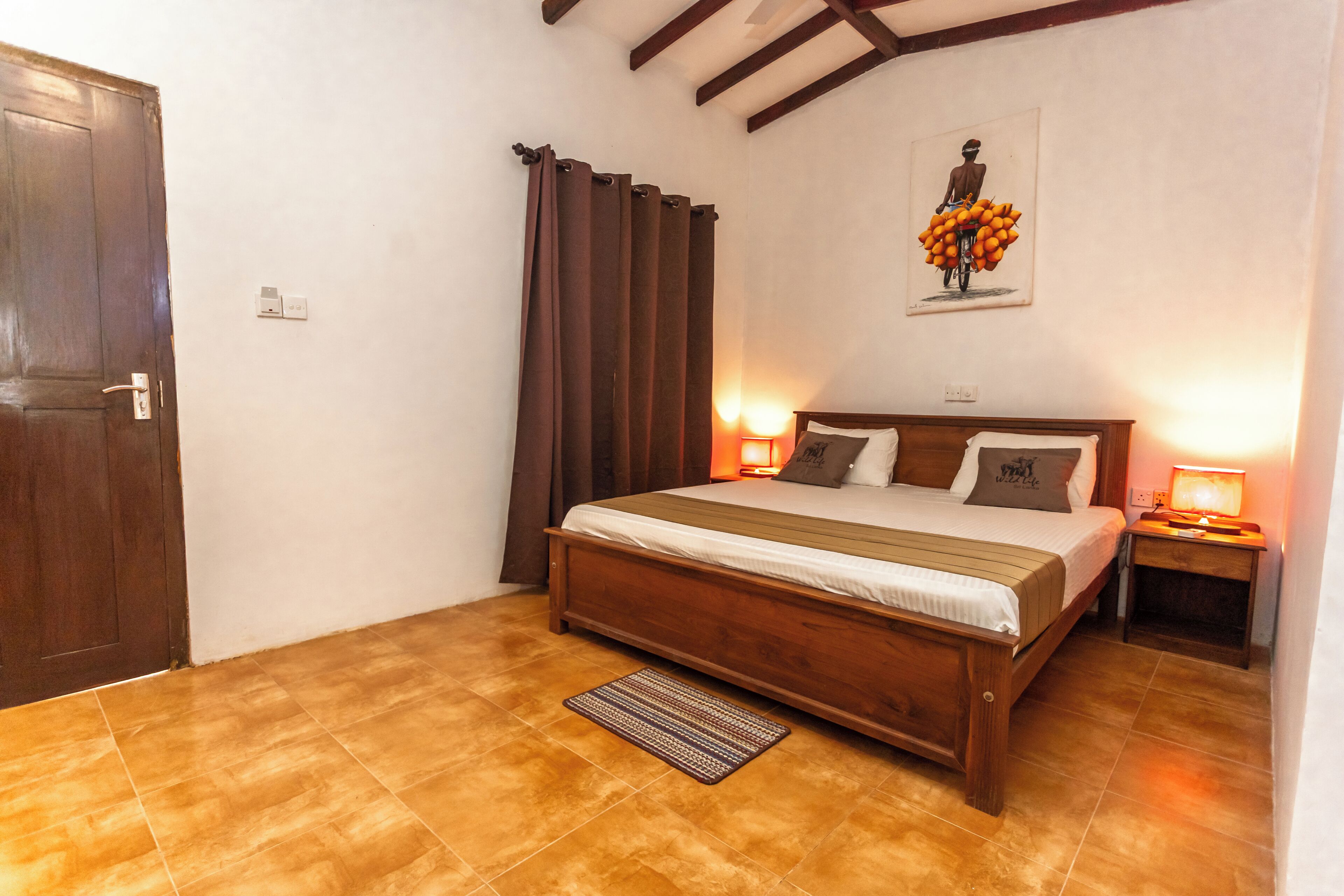 A bedroom with a wooden bed, a nightstand, a wall-mounted lamp, and a door.