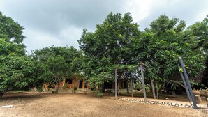 A courtyard with trees, a building with an orange facade, and a stone pathway. - Elephant Path by Alpine Resorts (Habarana)