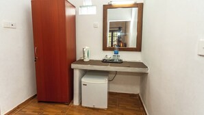 A compact bathroom with a wooden wardrobe, a small white refrigerator, a mirror, and a countertop with a bottle and a soap dispenser. - Elephant Path by Alpine Resorts (Habarana)