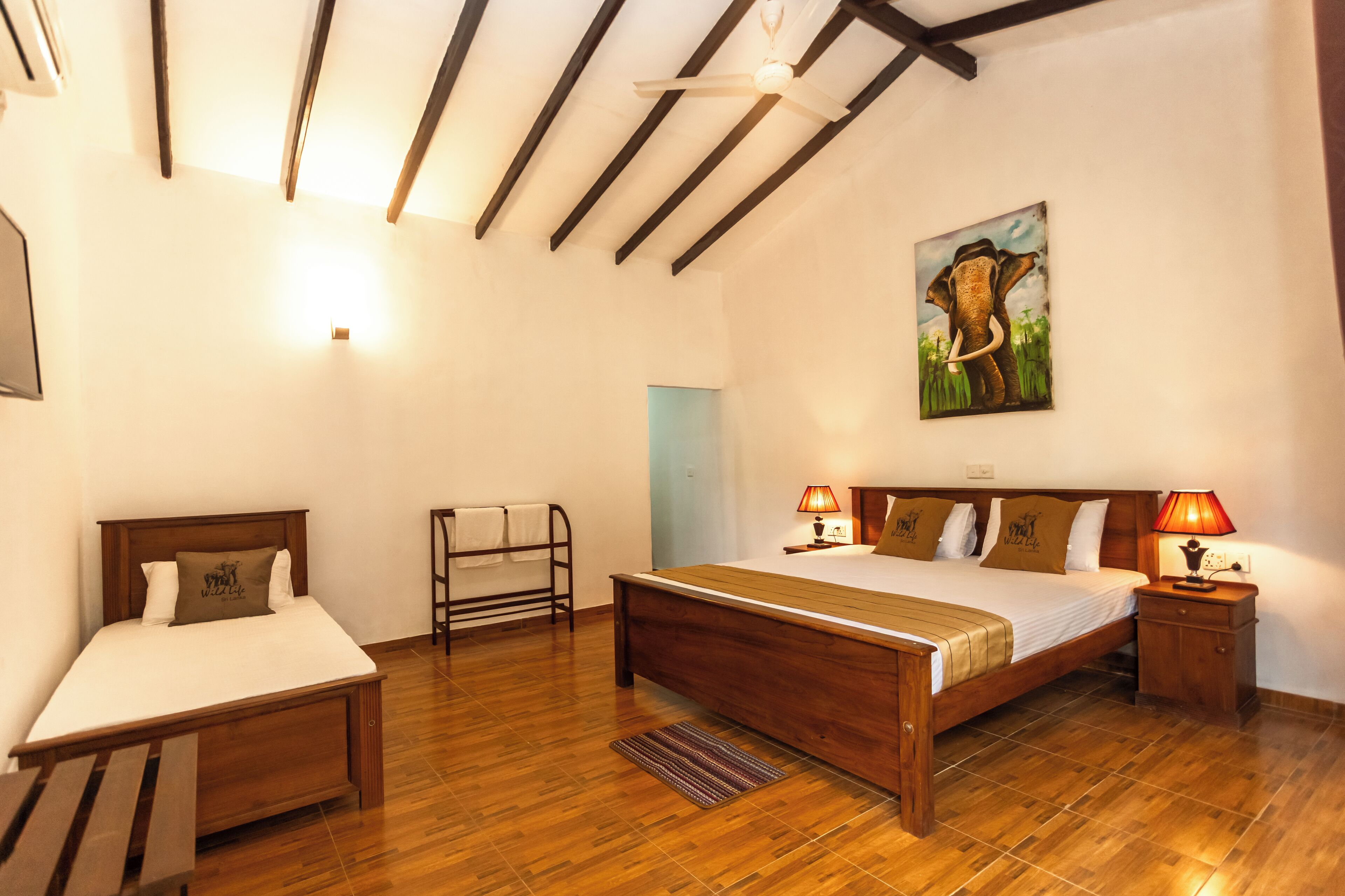 Un dormitorio con una cama de madera, una mesita de noche con lámpara, un cuadro en la pared y un banco de madera.