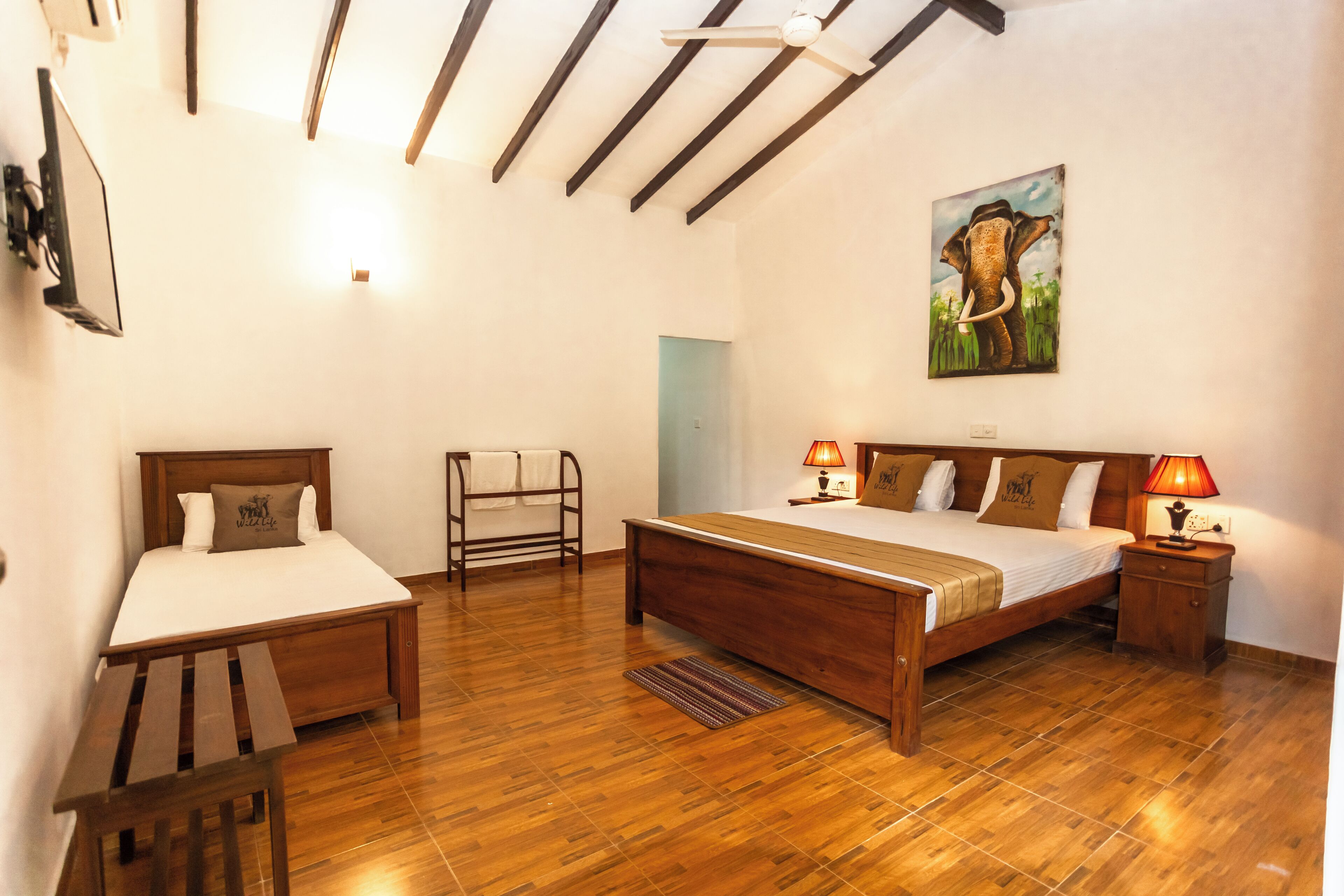 A bedroom with a wooden bed, a wooden bench, a nightstand with a lamp, and a painting on the wall.