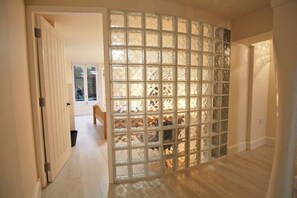 Een gang met een houten vloer, een glazen scheidingswand met een rasterpatroon, en een deur naar een andere kamer.