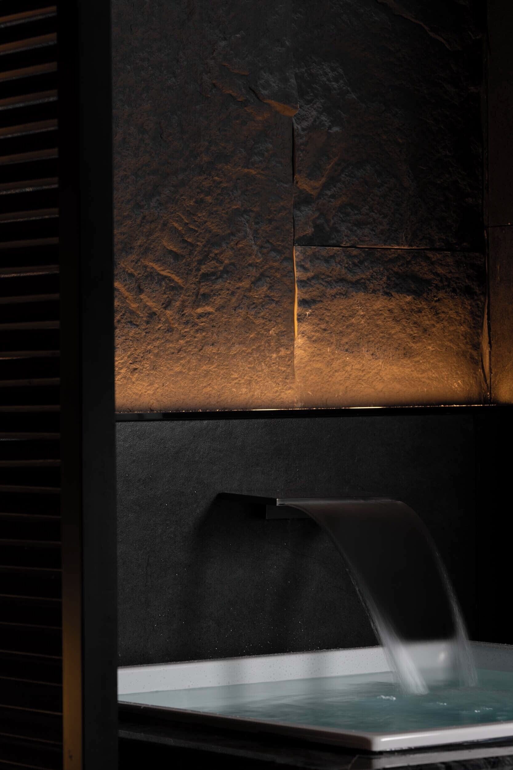 A spa area with a stone wall, a water feature, and a seating area.