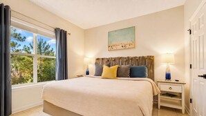 Une chambre à coucher avec un grand lit, deux tables de chevet, une fenêtre avec des rideaux, un tableau au mur et une porte.