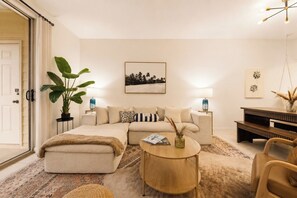 A modern living room with a sofa, coffee table, and a large plant. - Walk to Grand Blvd • Boho 2BR + Pool + Gym (Miramar Beach)