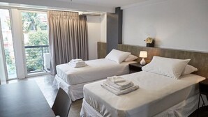 Una habitación de hotel con dos camas, un escritorio y un balcón con cortinas.