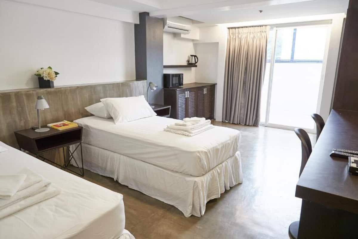 A hotel room with a bed, bedside table, lamp, and a desk with a chair.