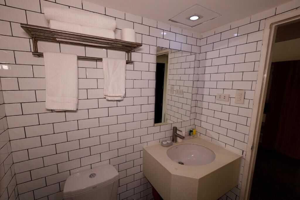 Une salle de bain avec des murs recouverts de carreaux blancs, un lavabo blanc et des toilettes.