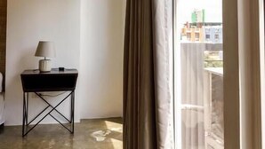 Una habitación con un ventanal grande, una mesita con una lámpara y suelo de hormigón.