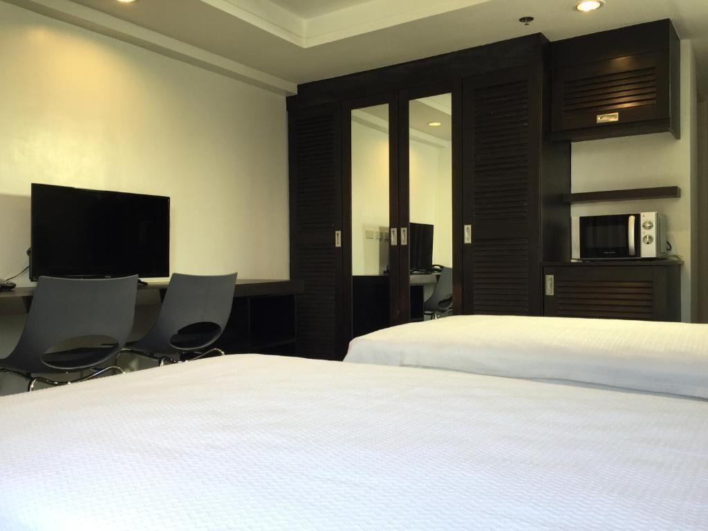 Une chambre d’hôtel avec deux lits, un bureau avec des chaises, une télévision et un four à micro-ondes.