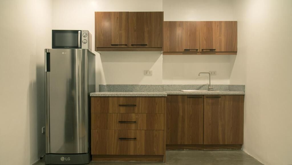 A compact kitchen with a stainless steel refrigerator, wooden cabinets, a granite countertop, and a sink.