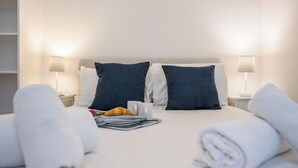 Un lit bien fait, avec des draps blancs, deux oreillers bleu foncé et une serviette pliée posée sur le côté.