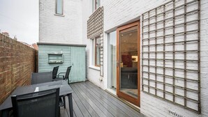 Une terrasse avec une table et des chaises, une porte bleue et un mur en briques blanches avec une fenêtre.
