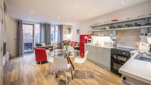 Une cuisine moderne avec un coin repas, un réfrigérateur rouge et une table en verre avec des chaises.