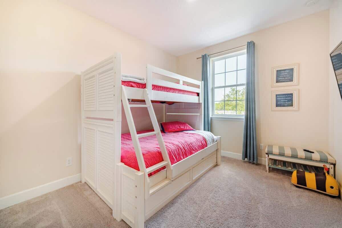 Une chambre avec des lits superposés, une fenêtre avec des rideaux et un petit banc avec un coussin à rayures.