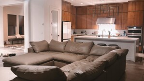 Ein modernes Wohnzimmer mit Ecksofa, einer Küchenzeile mit Holzschränken und einem Deckenventilator.