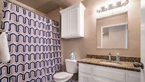 A bathroom with a patterned shower curtain, a toilet, a vanity with a mirror, and a sink with soap dispensers. - Top Floor - Spacious 2 Bed - Reserved Parking (Oklahoma City)