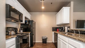 A compact kitchen with white cabinets, a stainless steel refrigerator, a microwave, and a stove. - Top Floor - Spacious 2 Bed - Reserved Parking (Oklahoma City)
