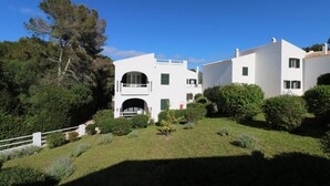 Uma villa branca com um arco central, rodeada por vegetação exuberante e uma cerca branca.