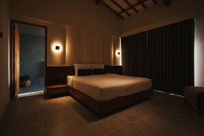Un dormitorio con cama, lámparas de noche, una mesita de noche, una silla y vistas al exterior a través de una ventana.