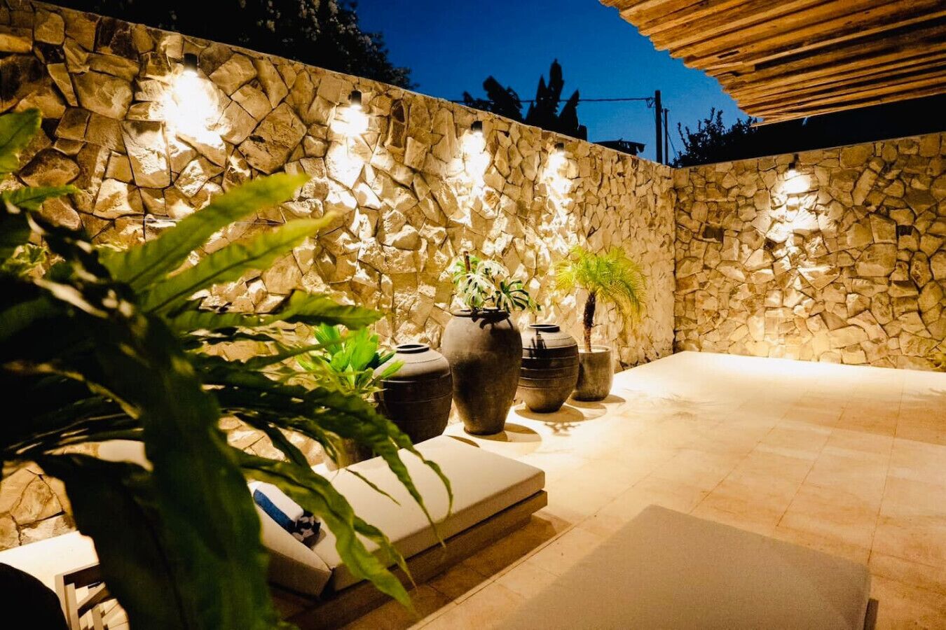A stone wall with built-in lighting, a seating area with cushions, and potted plants.