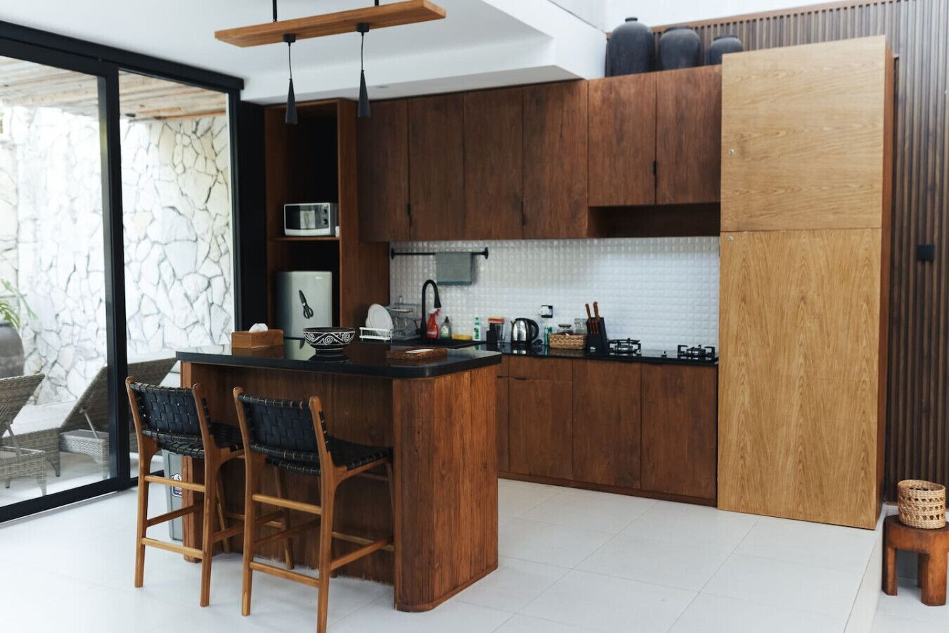 A modern kitchen with wooden cabinets, a central island with bar stools, a stove, and a large window.