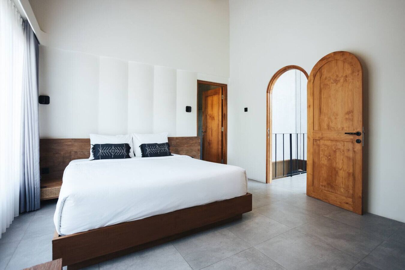 A modern bedroom with a large bed, wooden headboard, and a wooden door.