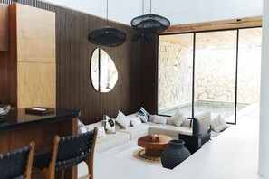 En moderne stue med sofa, sofabord, spiseplads med stole og et stort vindue med udsigt til en stenvæg.