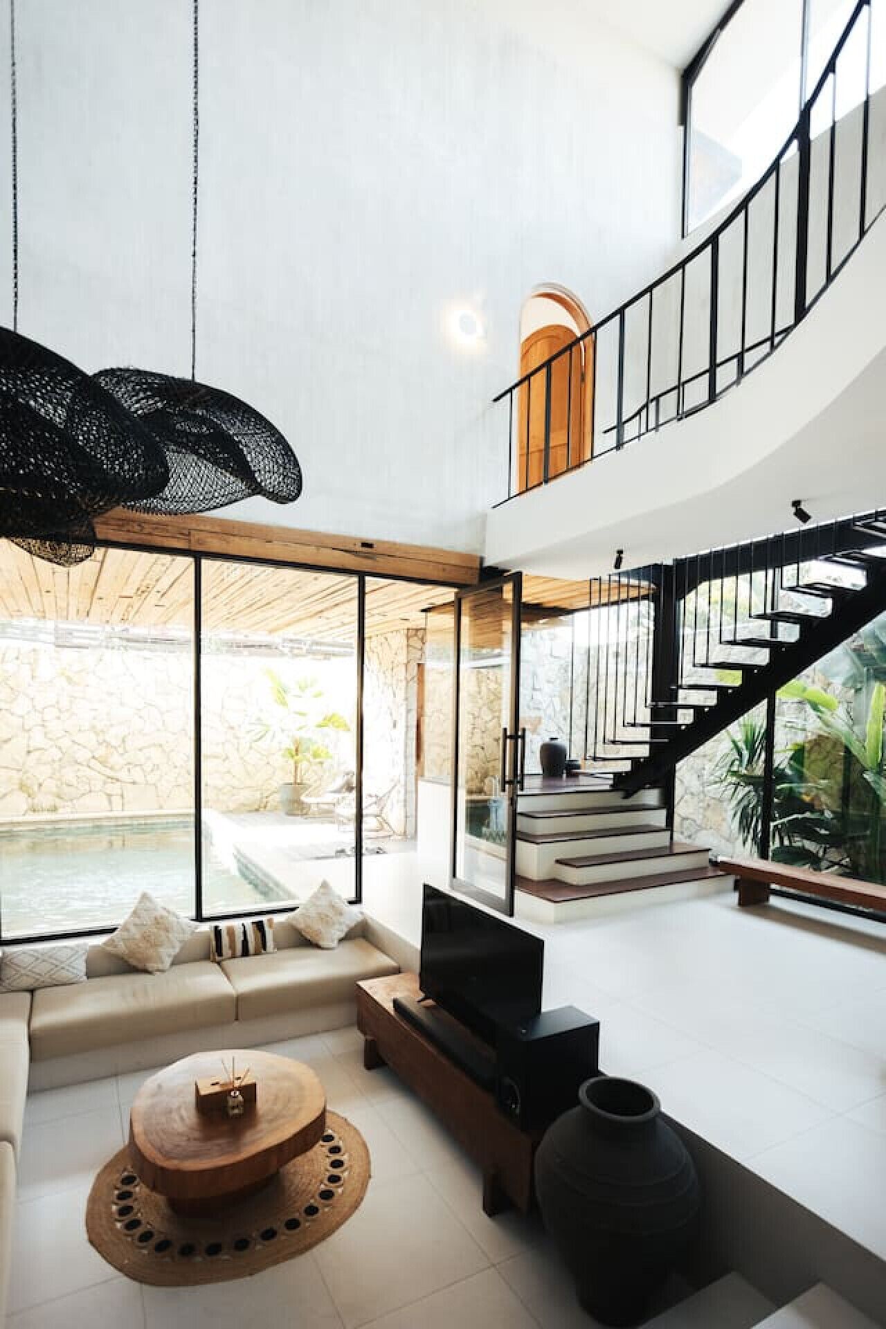 A modern living room with a TV, sofa, and coffee table, a staircase, and a view of a pool.